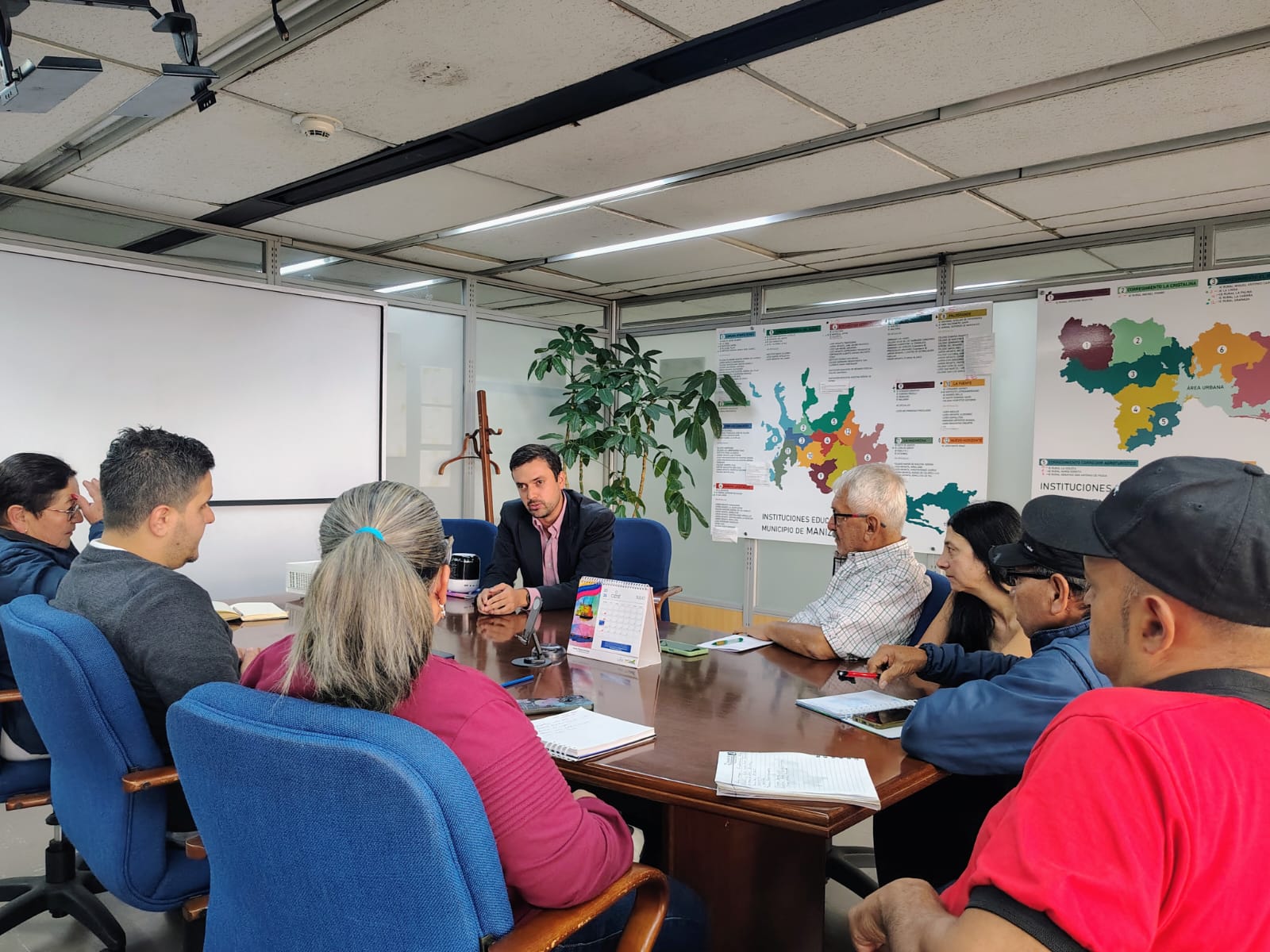 Reunión en sala de juntas del Área Metropolitana con ediles y líderes comunitarios alrededor de mesa con mapas territoriales de fondo