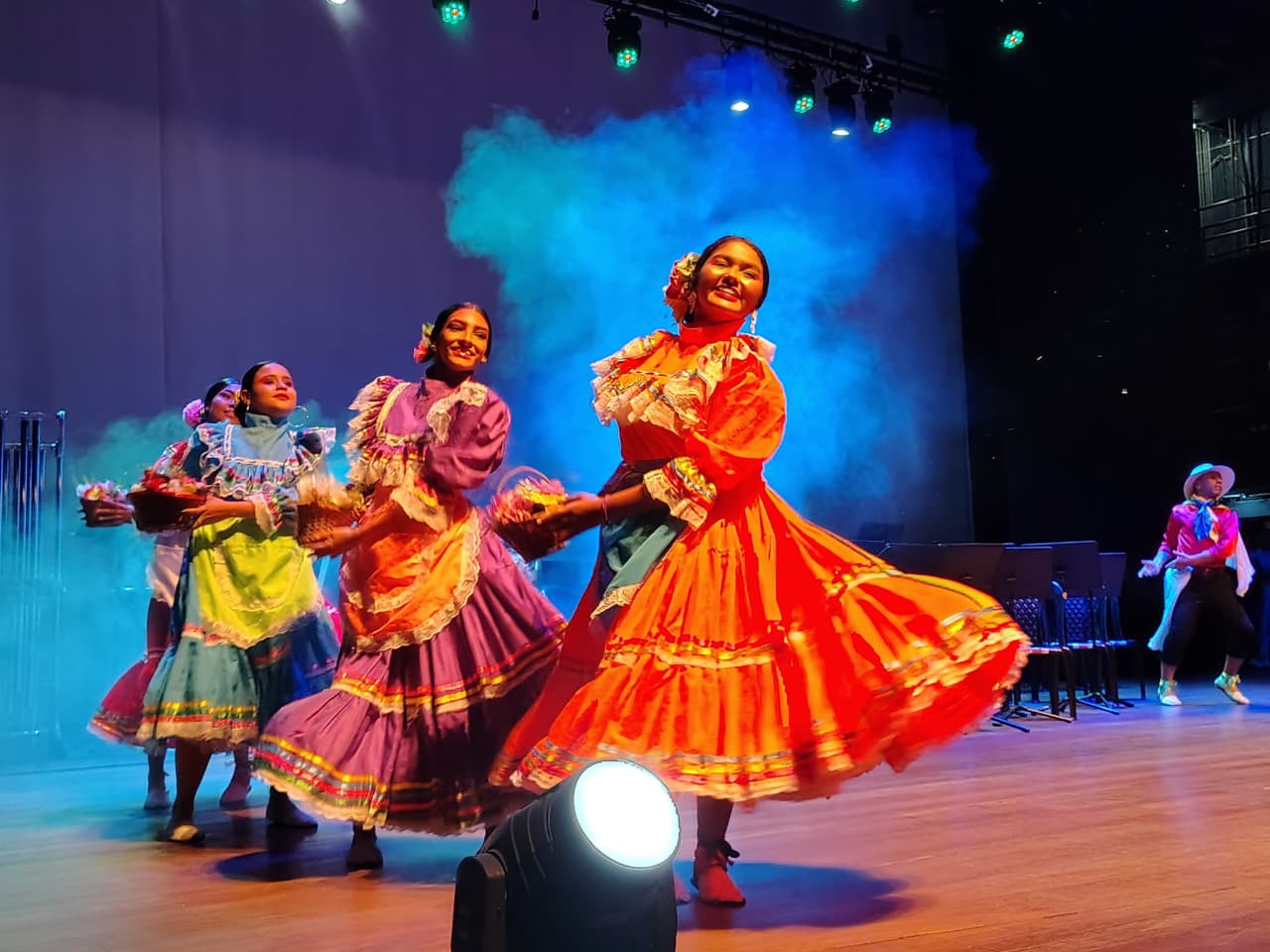 Bailarinas con trajes folclóricos colombianos coloridos danzando en escenario con luces y humo durante el primer festival de bandas metropolitanas